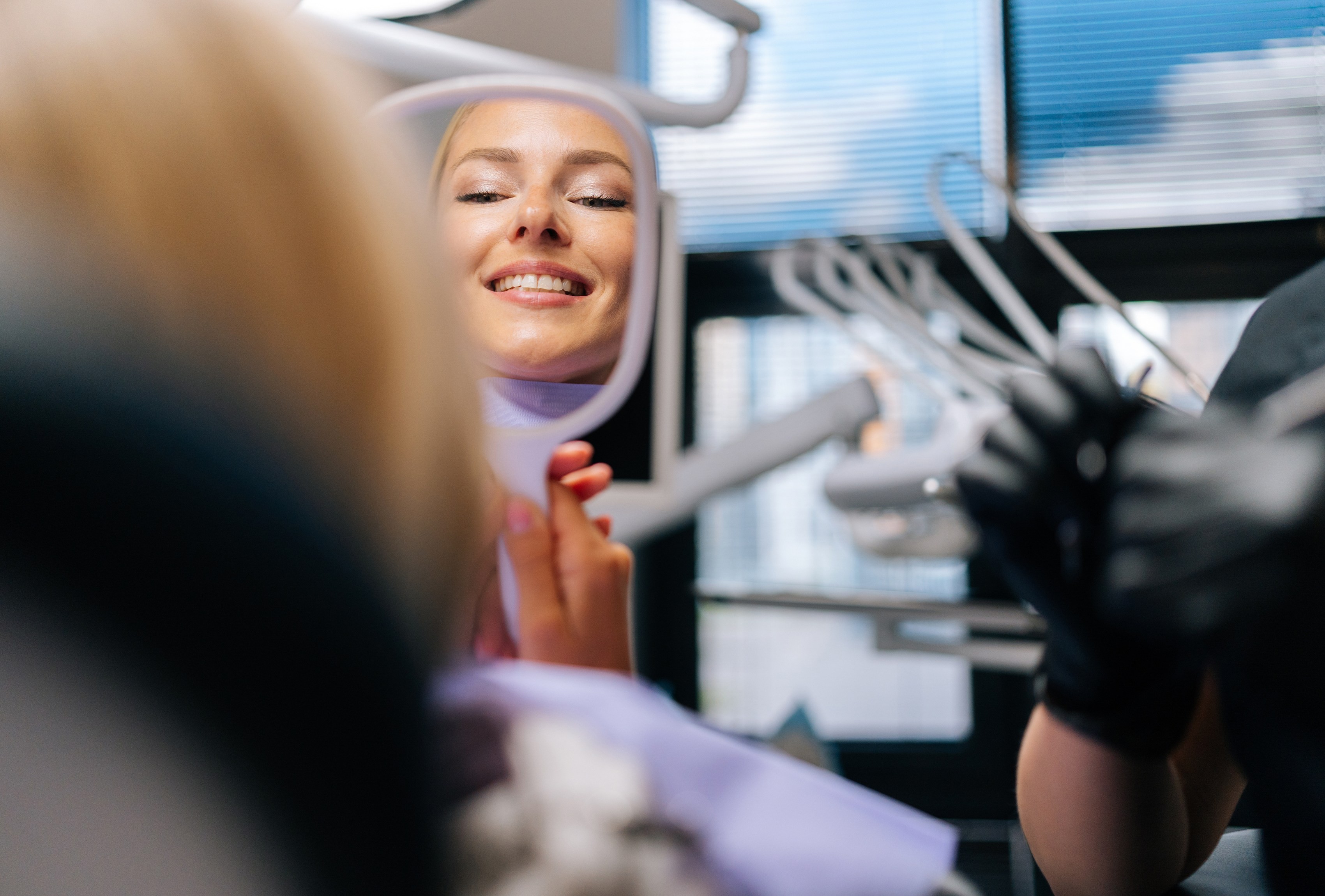 Woman smiling into a dental mirror while a dental professional works, representing our cosmetic dental services.