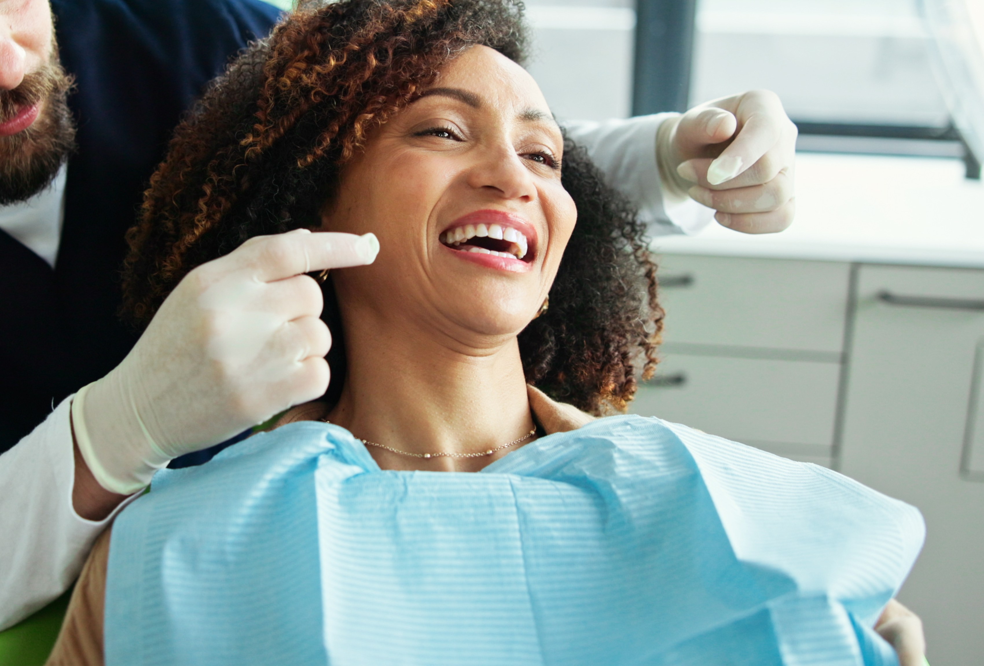 Smiling woman sitting in a dental chair with a friendly dentist pointing during a dental appointment.