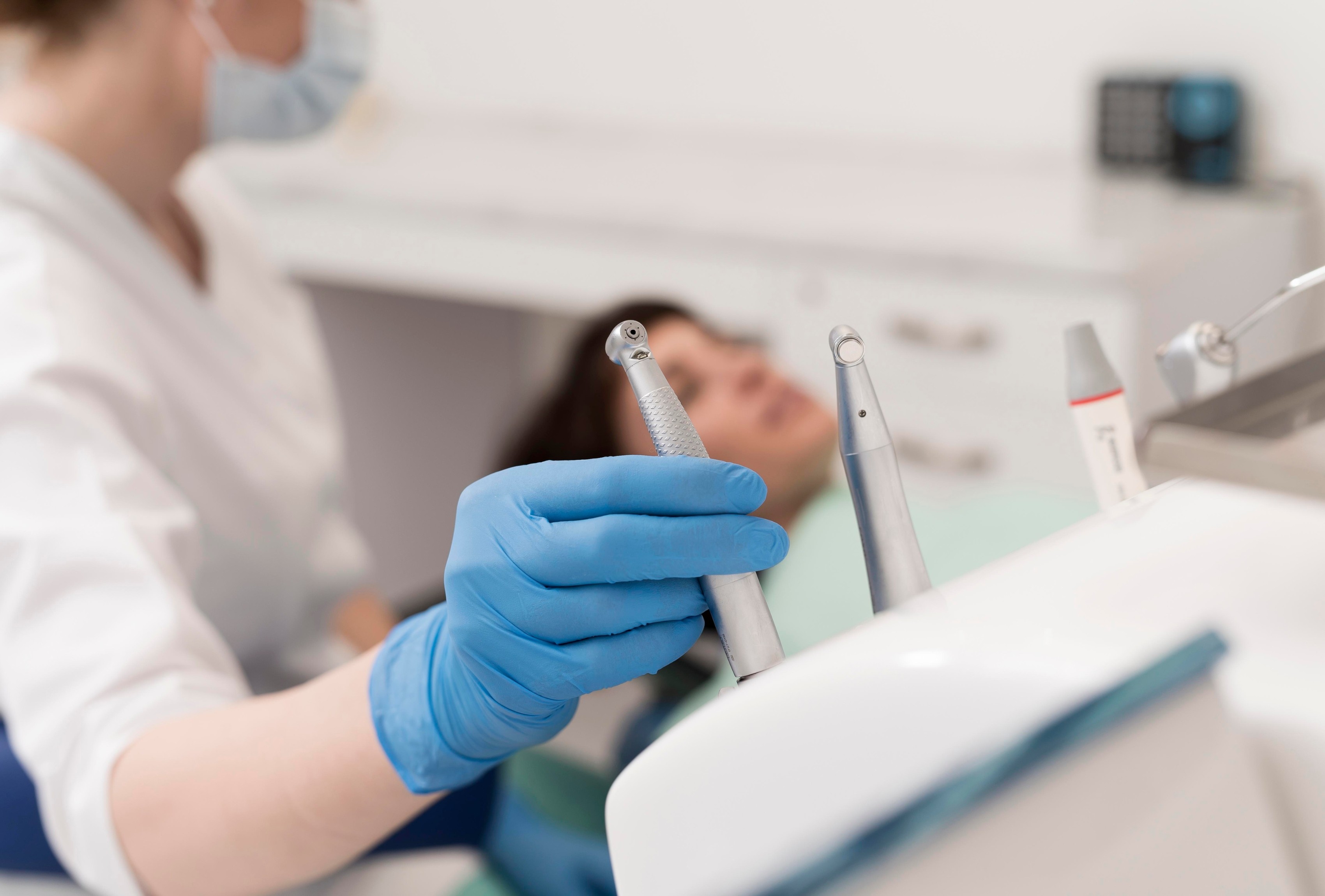 Dental professional with gloved hand holding dental instruments while a patient waits, representing our gentle care for patients overcoming dental anxiety.